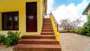 A set of outdoor stairs leading to a building with a yellow facade and a dark brown door. - Via Yellow Mist Home Stay (Kodaikanal)
