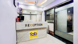 A reception area with a marble counter labeled "RECEPTION" and "fab hotels" logo, a ceiling fan, and a glass door leading to a room. - Fabhotel Anjani (Ahmedabad)