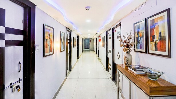 A hotel hallway with framed artwork on the walls, a reception desk with a vase and books, and a clean, tiled floor. - Fabhotel Anjani (Ahmedabad)