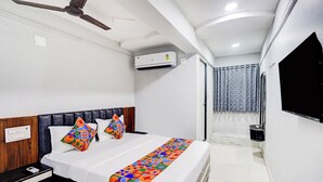A hotel room with a bed, a nightstand, a ceiling fan, an air conditioning unit, a shower area with a curtain, and a mounted TV. - Fabhotel Anjani (Ahmedabad)