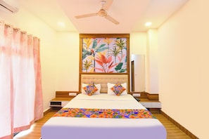 A hotel room with a bed, a ceiling fan, a painting, and a nightstand.