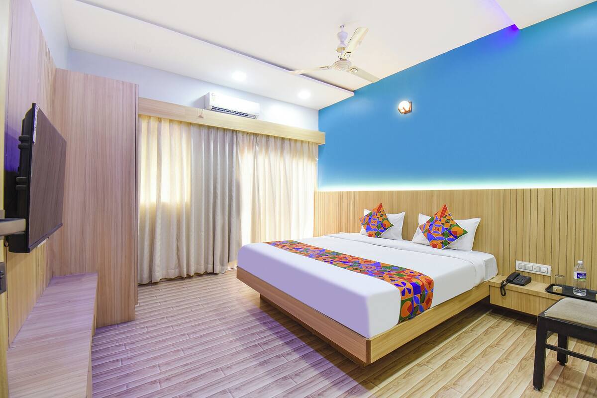 A hotel room with a bed, a desk, a telephone, and an air conditioning unit.
