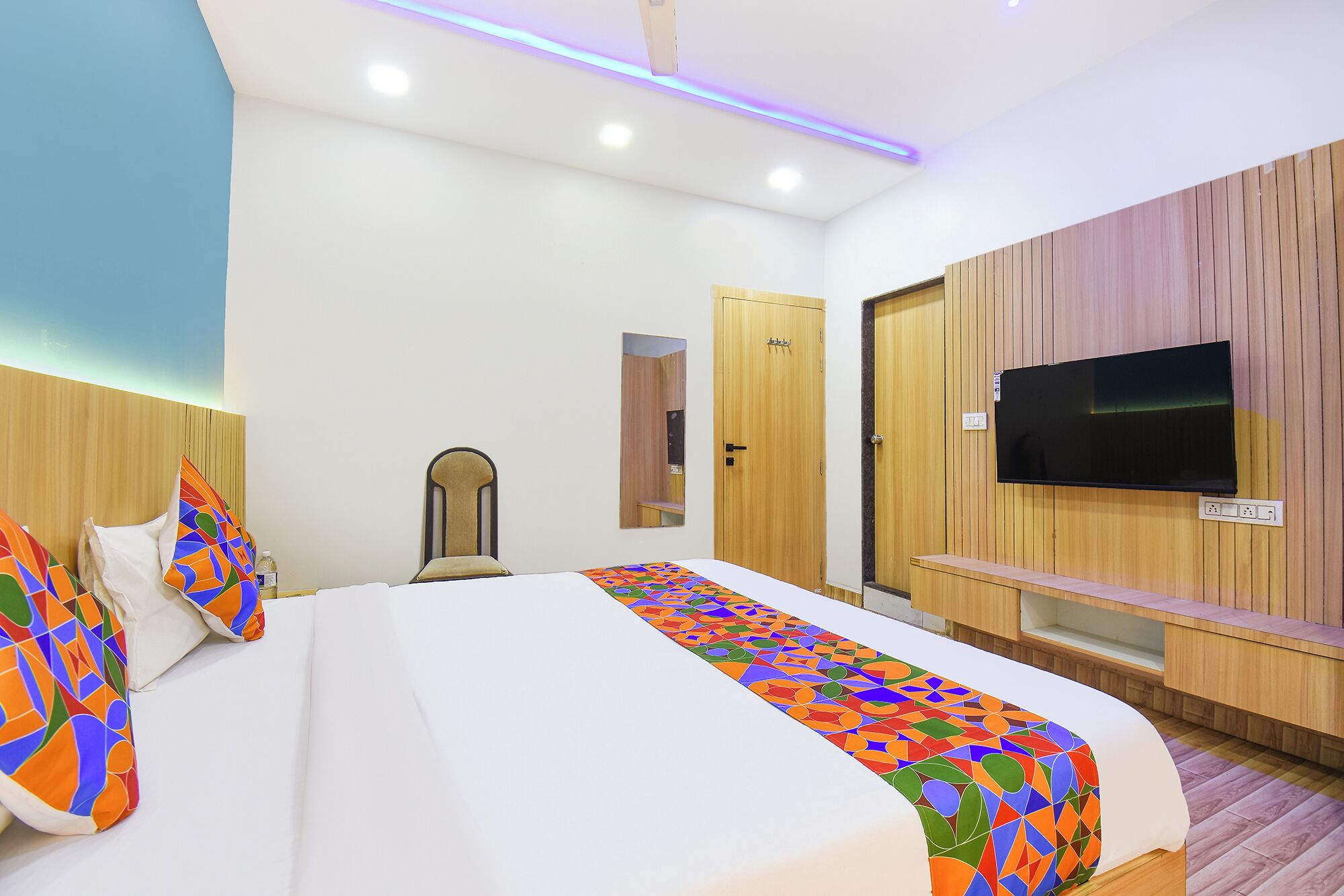 A hotel room with a bed, a TV, a wooden wardrobe, and a small seating area.