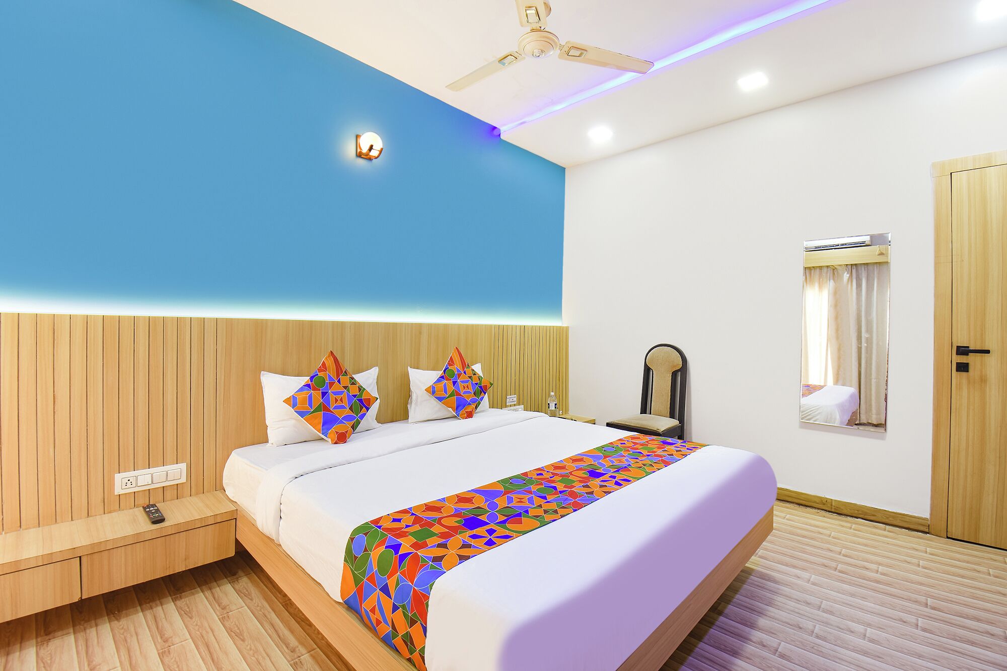 A hotel room with a bed, wooden headboard, ceiling fan, bedside table, and a window with curtains.