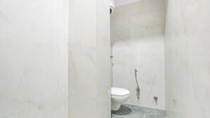 Une petite salle de bain étroite, carrelée de carreaux blancs, et équipée d’une seule toilette.
