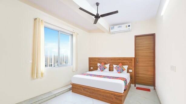 Une chambre à coucher comprenant un lit, un ventilateur de plafond, un appareil de climatisation, une fenêtre avec des rideaux et une porte en bois.