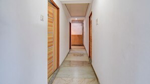 Un couloir étroit, avec des portes en bois de chaque côté, un sol carrelé et un plafond avec des poutres en bois.