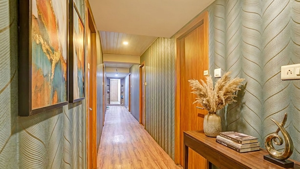 A hallway with wooden flooring, patterned wallpaper, and a wooden console table with decorative items. - Via Maahi Residency (Mumbai)
