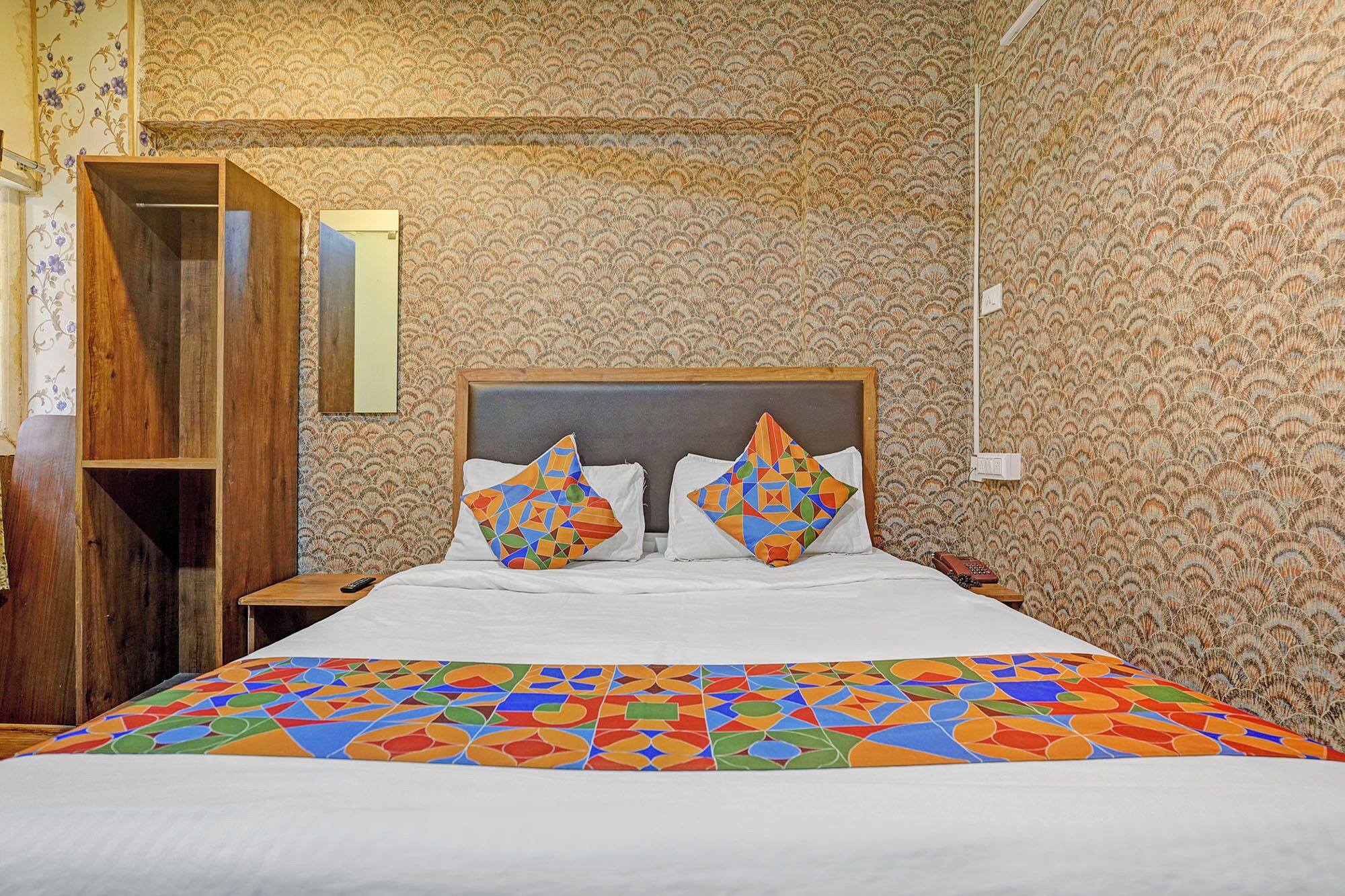 Una habitación de hotel con una cama grande, dos almohadas, una mesita de noche de madera y un espejo.