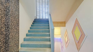 A staircase with blue steps leading upwards, flanked by a textured wall on the left and a wall with geometric wall art on the right. - Via Maahi Residency (Mumbai)