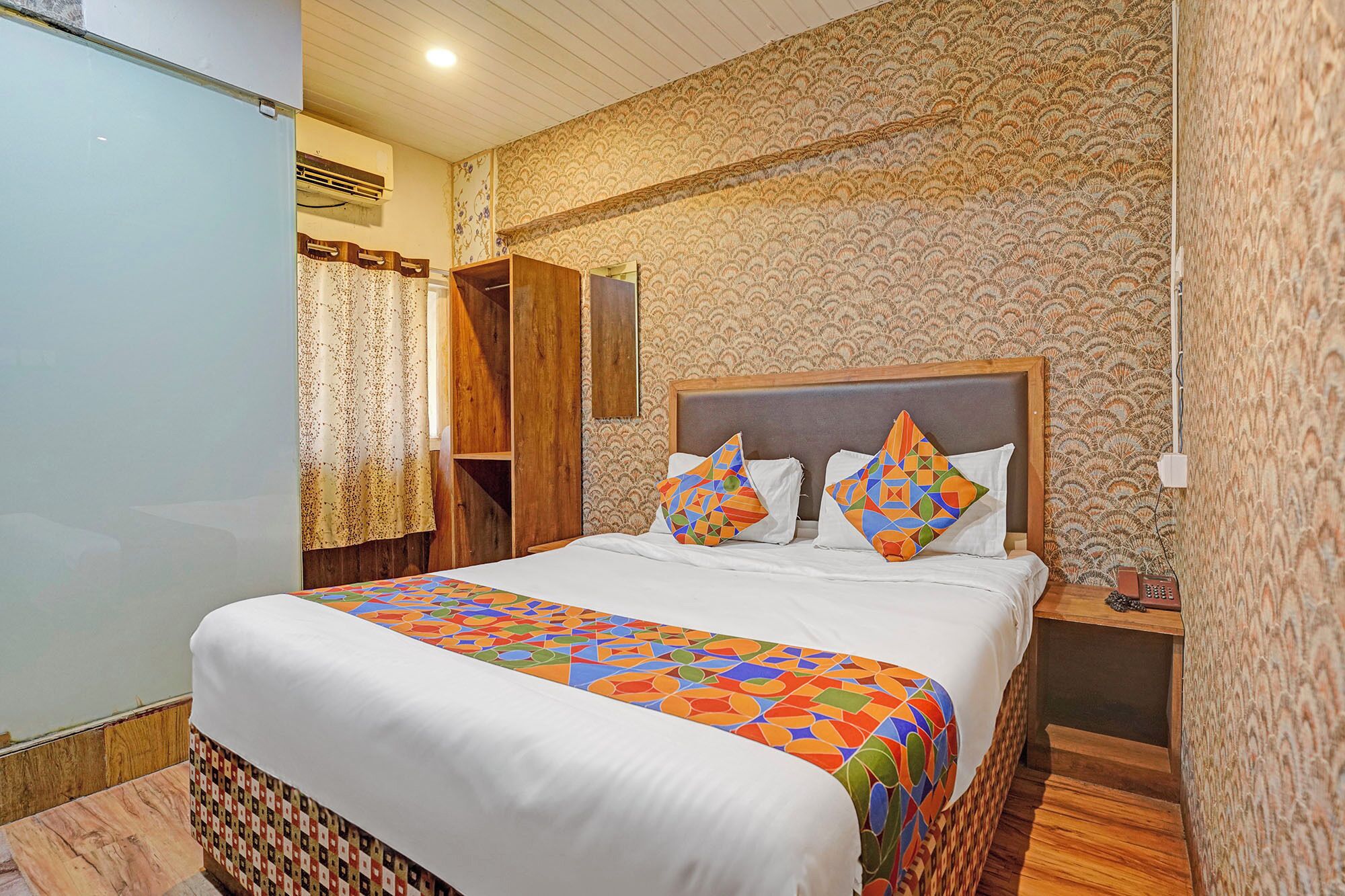 A neatly made bed with a colorful bedspread, a wooden headboard, and two decorative pillows.