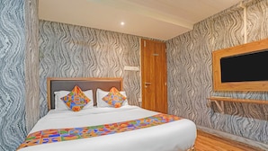 A bedroom with a bed, patterned wallpaper, a wooden door, and a mounted TV. - Via Maahi Residency (Mumbai)