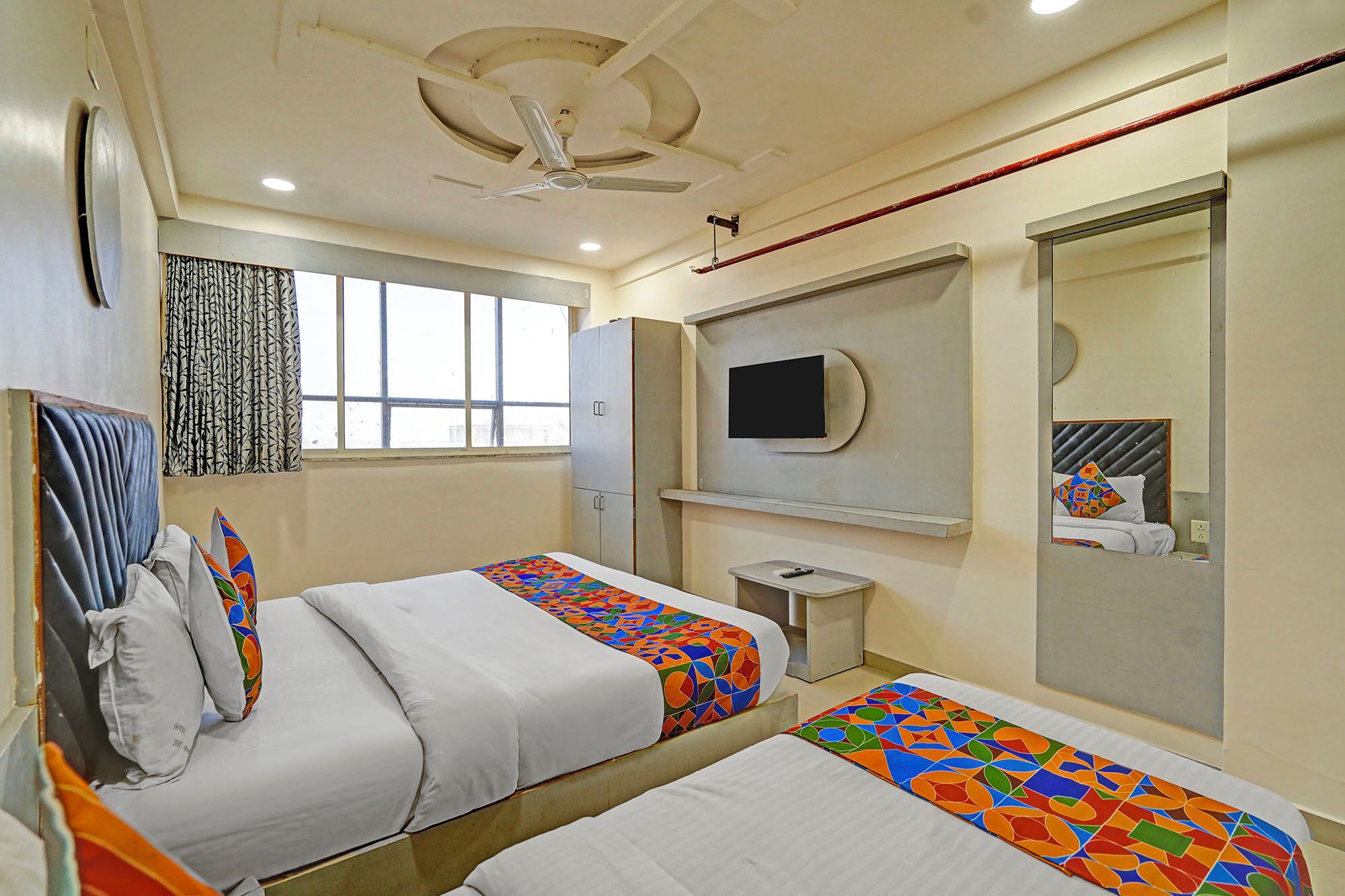 A hotel room with two beds, a ceiling fan, a TV, and a large mirror.