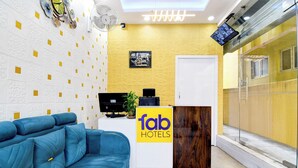 A hotel reception area with a blue sofa, a reception desk, a TV, and a yellow wall. - Fabhotel Florence Palace (Kolkata)