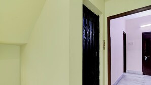 A hallway with a black door, a light switch, and a marble floor. - Fabhotel Florence Palace (Kolkata)