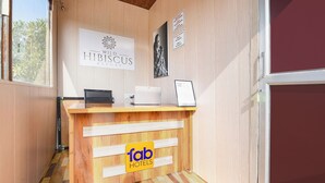 A reception desk with a wooden finish, a laptop, and a framed picture on the wall. There is a sign for 'Wild Hibiscus Resort' and another sign with 'Home rules'. - Fabhotel Wild Hibiscus Resort (Ramnagar)