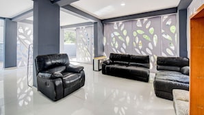 A spacious living area with a black leather sofa and a recliner, a decorative wall with leaf patterns, and a wooden door. - Fabhotel Rajyog Residency (Pune)