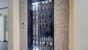 A modern elevator with a geometric metal gate, a marble wall, and a visible floor number panel. - Fabhotel Heaven 75 (Hyderabad)