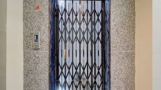 An elevator with a metal security gate and a control panel with a red emergency button. - Fabhotel Heaven 75 (Hyderabad)