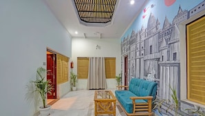 A living room with a blue sofa, wooden coffee table, and a mural of a building on the wall. - Fabhotel Om Sai Residency (Varanasi)