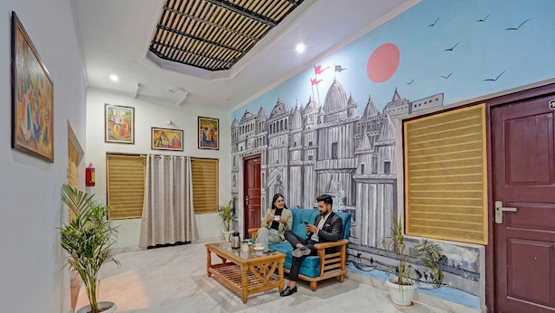 A room with a mural of a cityscape, a wooden sofa, a coffee table, and potted plants. - Fabhotel Om Sai Residency (Varanasi)