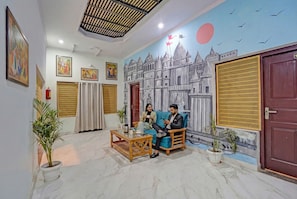 A room with a mural of a cityscape, a wooden sofa, a coffee table, and potted plants. - Fabhotel Om Sai Residency (Varanasi)