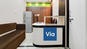 A reception desk with a 'Via' sign, a brown sofa, a refrigerator, and a wooden wall. - Via Rajdanga Retreat (Kolkata)