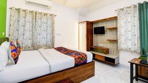 A bedroom with a bed, a TV mounted on a wooden wall, and a ceiling fan. - Via Rajdanga Retreat (Kolkata)