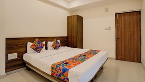 A neatly made double bed with a colorful geometric-patterned bedspread and pillows, a wooden headboard, a wooden wardrobe, and a wooden door. - FabHotel Purple Grand - Jalahalli West (Bangalore)