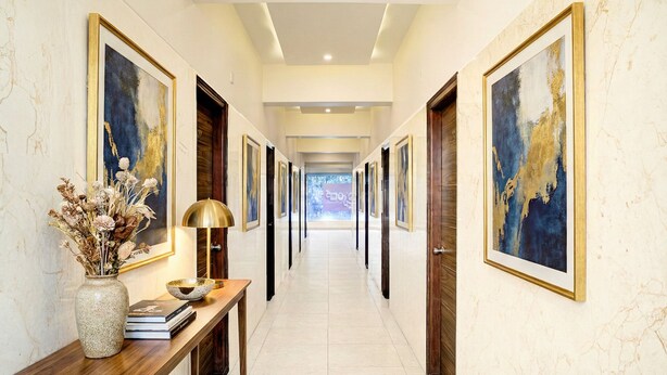 A hallway with framed artwork on the walls, a wooden console table with a vase and books, and a modern ceiling design. - FabHotel Purple Grand - Jalahalli West (Bangalore)