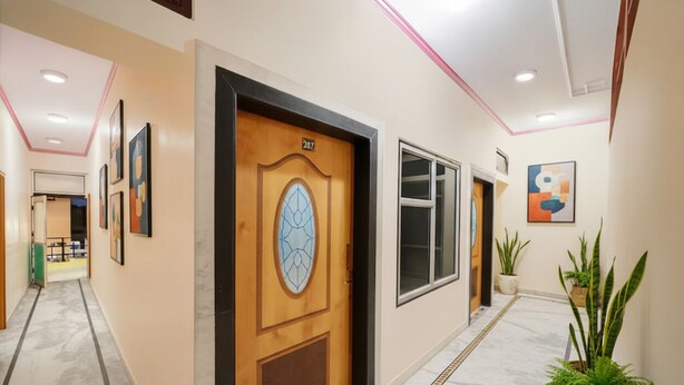 A hallway with a wooden door labeled '207', a marble floor, and potted plants. - Via Mansagar (Jaipur)