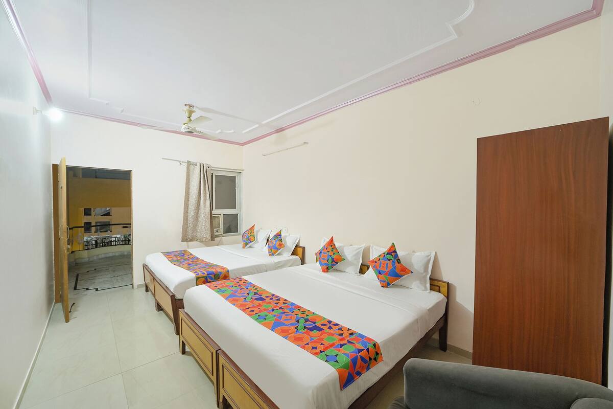 A hotel room with two beds, a wooden wardrobe, a ceiling fan, and a window with curtains.