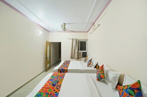 Habitación de hotel con dos camas, ventilador de techo, ventana con cortinas y puerta con un reloj.