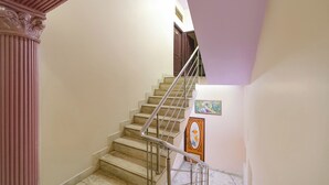 A staircase with marble steps and a metal railing, leading to a landing with a door and a framed picture. - Via Mansagar (Jaipur)