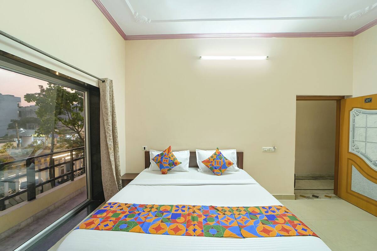A hotel room with a large window, a bed with a colorful bedspread, and a door with a number.