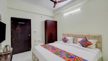 A hotel room with a bed, a ceiling fan, a desk with a kettle, and a TV.