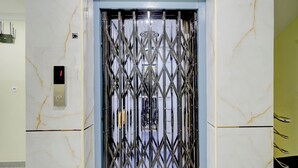 An elevator with a metal security gate, a control panel, and marble walls. - FabHotel Honey Grand - 400m From Yashoda Hospitals, Hitech City. (Hyderabad)