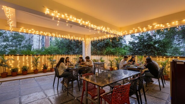 An outdoor dining area with string lights, potted plants, and people dining. - FabHotel Honey Grand - 400m From Yashoda Hospitals, Hitech City. (Hyderabad)