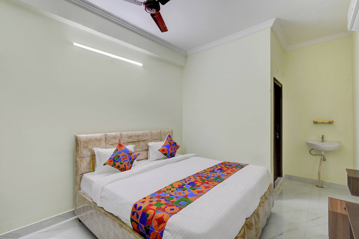 A bedroom with a bed, pillows, a bedside table, a nightstand, a ceiling fan, a window, and a bathroom with a sink.