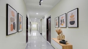 A hallway with framed artwork on the walls, a wooden console table with books and a vase, and a marble floor. - FabHotel Honey Grand - 400m From Yashoda Hospitals, Hitech City. (Hyderabad)