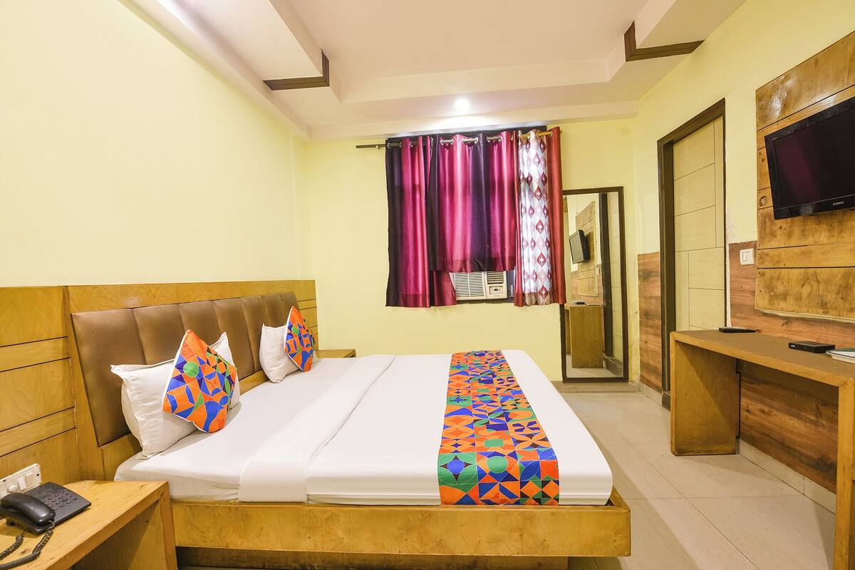 A hotel room with a bed, a bedside telephone, a TV, and a wooden desk.
