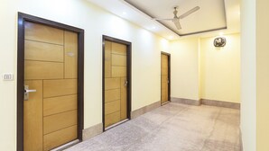 A hallway with three wooden doors, a ceiling fan, and a light fixture. - Fabhotel Golden Gate Deluxe (New Delhi)