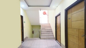 A hallway with a staircase leading to an exit, a fire extinguisher, and a door with a number plate. - Fabhotel Golden Gate Deluxe (New Delhi)