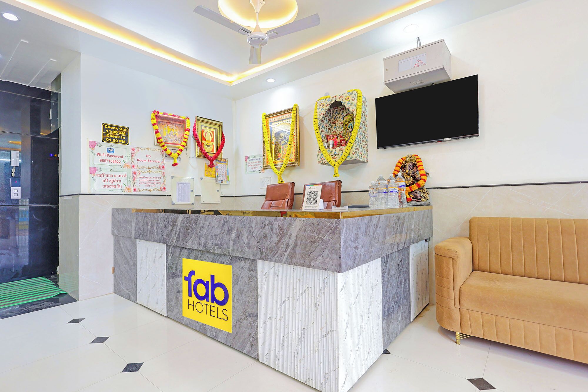 A hotel reception desk with a marble counter, a sofa, and a television mounted on the wall.
