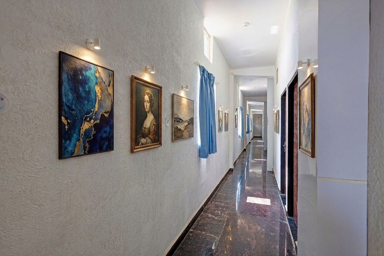 A hallway with artwork on the walls, a marble floor, and a view into another room.