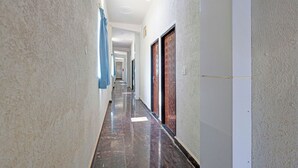 A long, narrow hallway with a polished floor, textured walls, and doors on one side. - Fabhotel Shri Hari Singh Dham (Vrindavan)