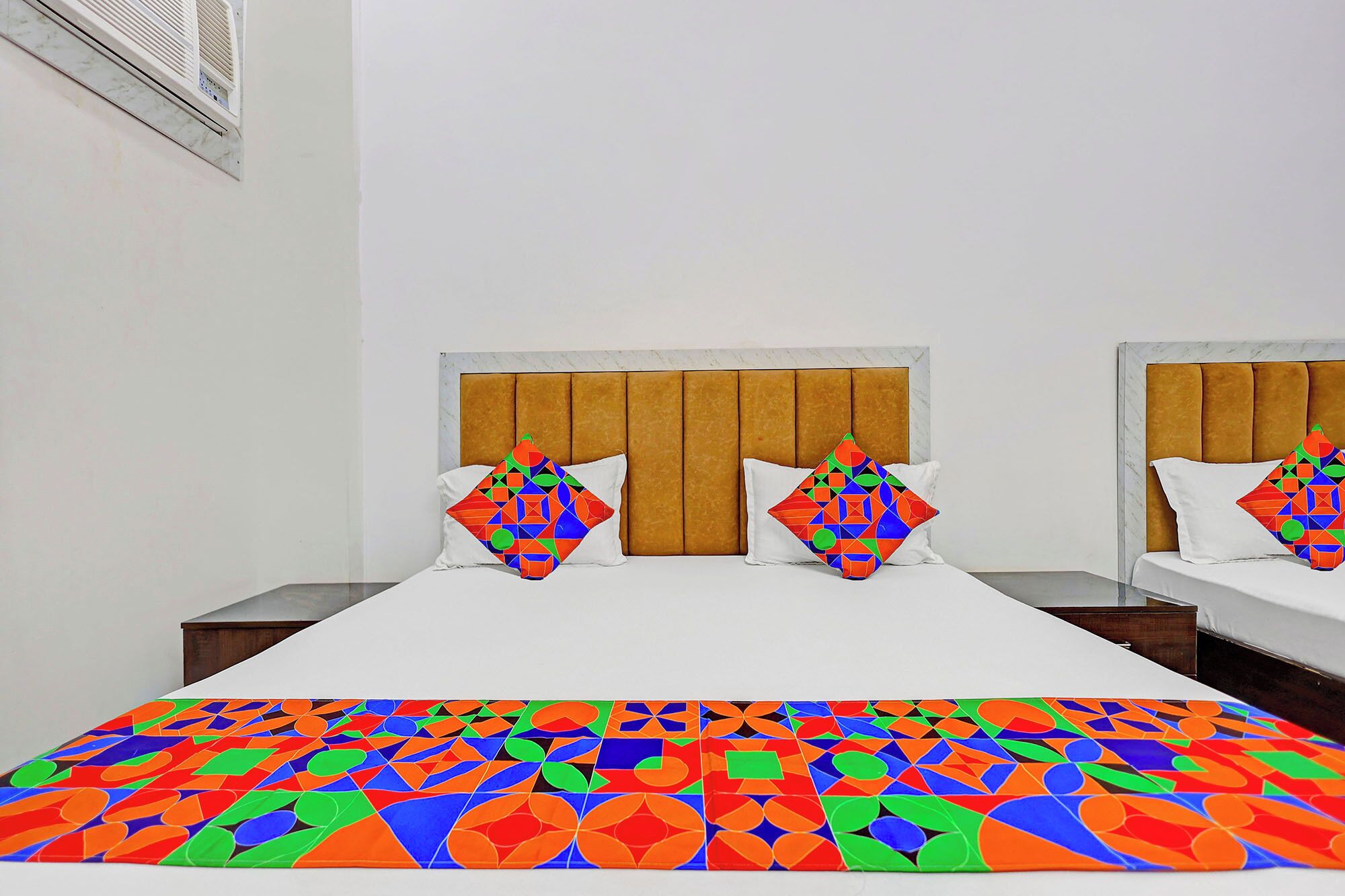A hotel room with a large bed, two nightstands, a headboard with a panel design, and a colorful geometric-patterned bedspread.