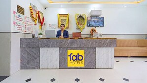 A hotel reception desk with a marble counter, a logo, and a sofa in the background. - Fabhotel Shri Hari Singh Dham (Vrindavan)