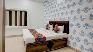 A bedroom with a wooden bed, white bedding, colorful pillows, and patterned wallpaper. - Via Atithi Inn (Varanasi)