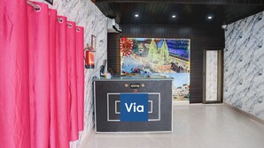 A reception area with a marble wall, a reception desk, and a large window displaying a cityscape. - Via Atithi Inn (Varanasi)